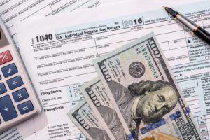 A calculator, tax documents, and tax refund money on a table.